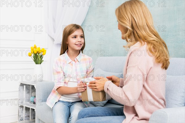 Daughter giving gift box mom sitting couch
