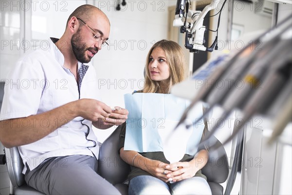 Dentist talking with female patient while working dental jaw