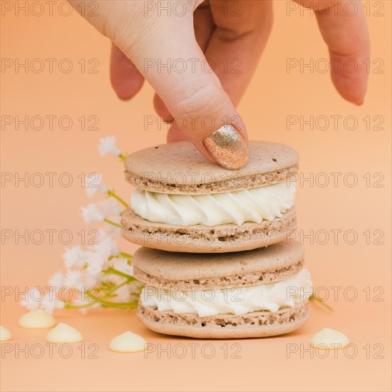 Female s hand with golden nail polish taking macaroon against colored backdrop