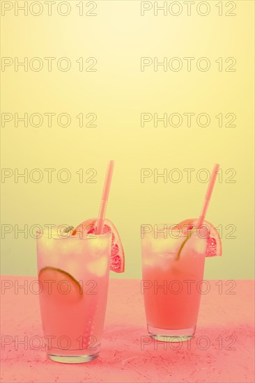 Fresh pink alcoholic cocktail with grapefruit lemon slice ice cubes against yellow background