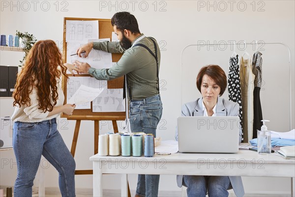 Front view female fashion designer working atelier with laptop colleagues