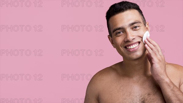 Front view smiley shirtless man using cotton pads his face