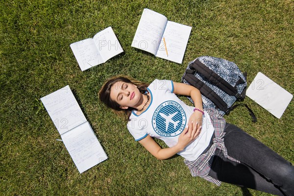 Girl lying grass surrounded by notebooks