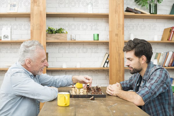 Happy aged man young guy playing chess table room