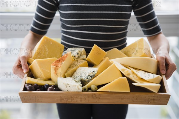 Mid section woman holding cheese slices wooden tray