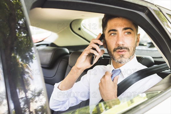 Modern man sitting car adjusting his neck tie talking mobile phone