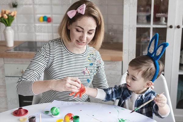 Mother teaching little boy how paint eggs easter