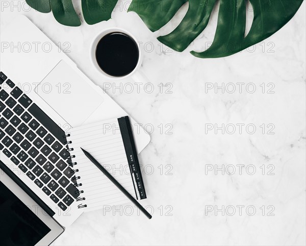 Overhead view diary pencil laptop coffee cup monstera leaf marble backdrop
