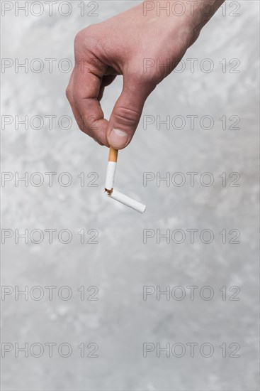 Persons hand holding broken cigarette old wall background