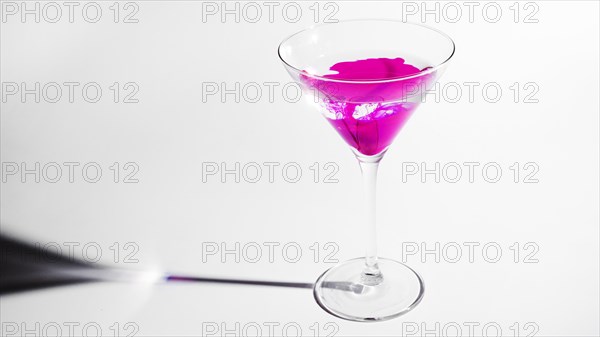 Pink ink dissolving martini glass isolated white backdrop