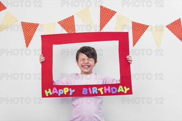 Portrait cute boy holding birthday frame with eyes closed