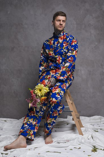 Portrait sad young man sitting stool with flower bouquet his hand