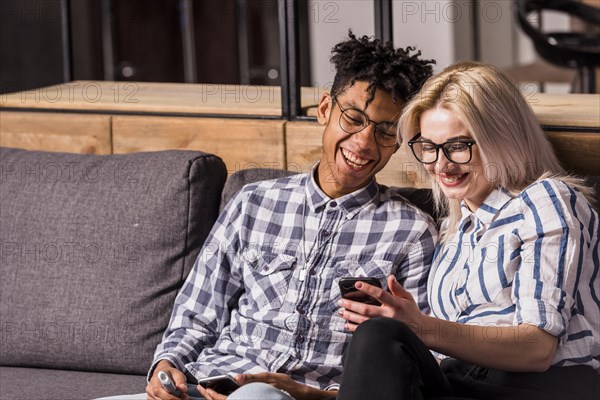 Portrait smiling young couple sitting sofa looking mobile phone