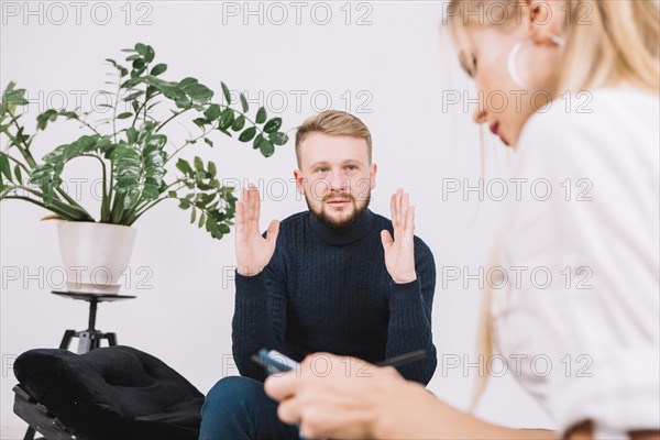 Sad young man discussing her problems with female psychologist clinic