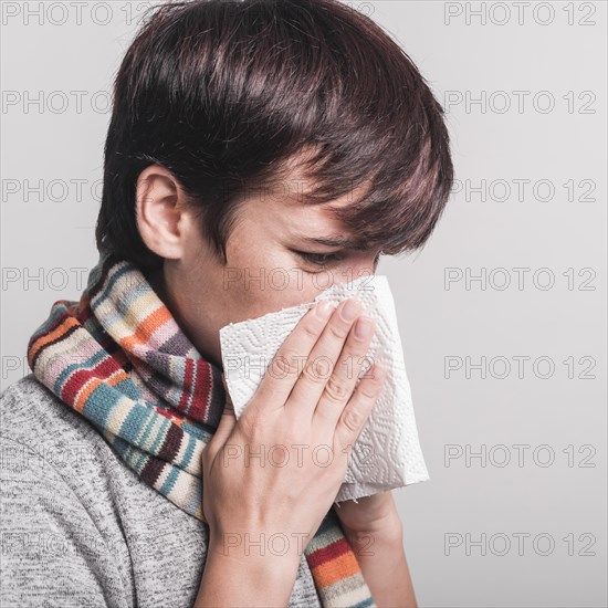 Sick woman blowing nose tissue paper against gray background