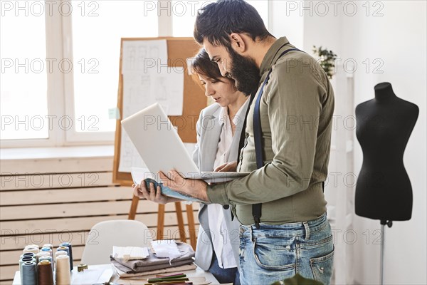 Side view fashion designers working atelier with laptop