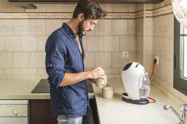Side view man standing kitchen holding coffee mug