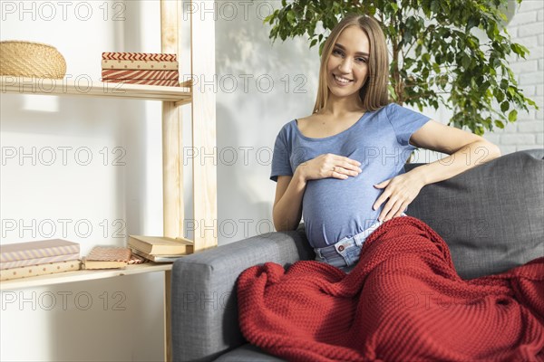 Smiley pregnant businesswoman sitting couch holding her belly