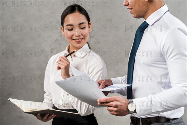 Smiling portrait young businesswoman holding diary hand looking documents hold by her colleague