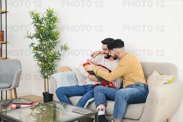 Smiling young gay couple sitting sofa loving their baby