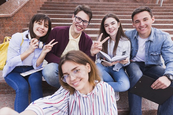 Students sitting stairs gesturing two fingers looking camera