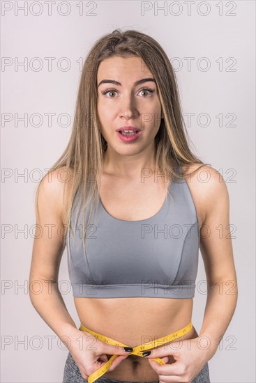Surprised attractive slim woman measuring waist