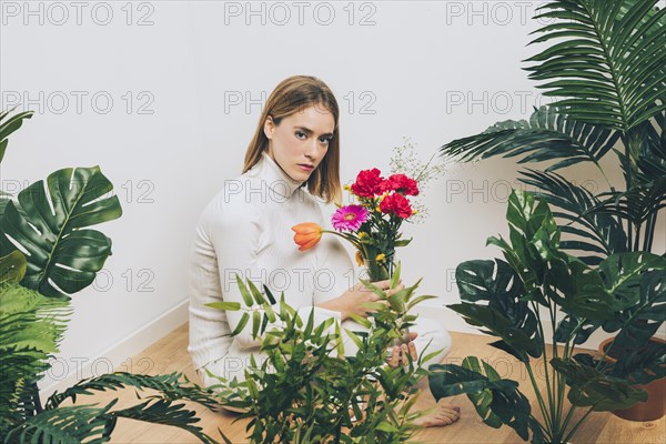 Thoughtful woman sitting with flowers near green plants