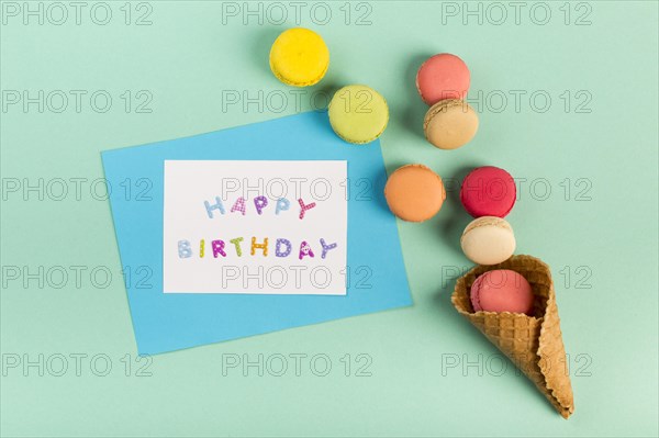 Waffle cone with macaroons near happy birthday card mint green backdrop