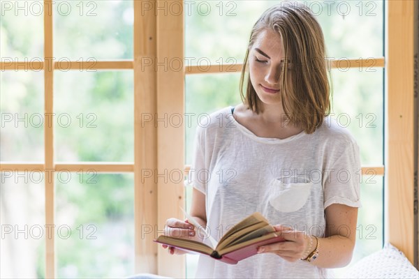 Woman standing front window reading book