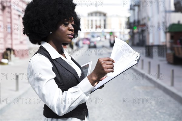 Young african businesswoman standing road reading document clipboard