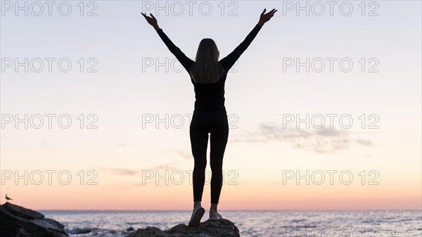 Back view woman standing coast with her arms up