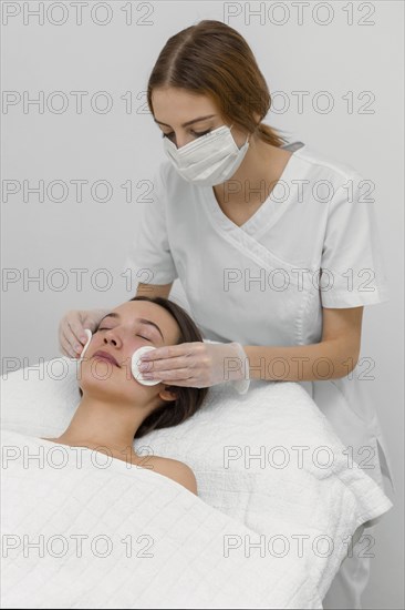 Beautician with female client salon face care routine with cleansing disks