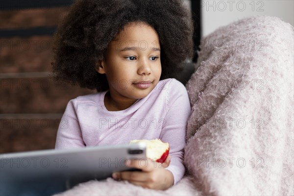 Little girl eating apple using tablet