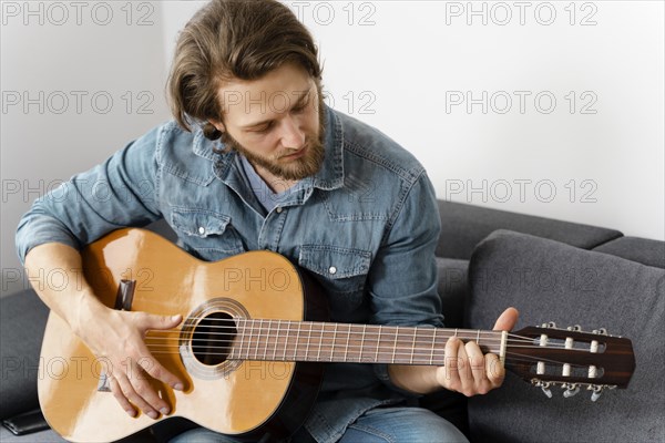 Medium shot man playing guitar couch