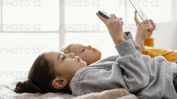 Siblings bed playing mobile tablet