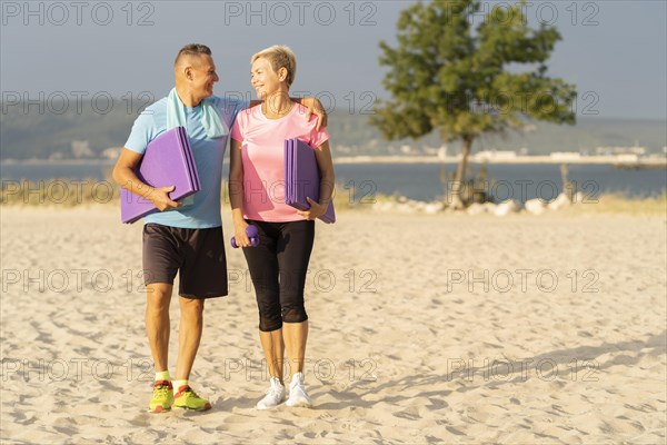 Smiley senior couple with working out equipment beach copy space