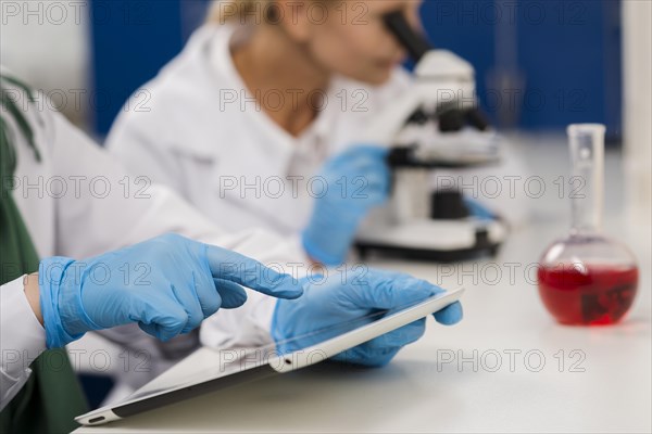 Side view female scientists lab working with microscope tablet