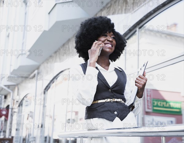 Young african businesswoman standing outside building talking smart phone