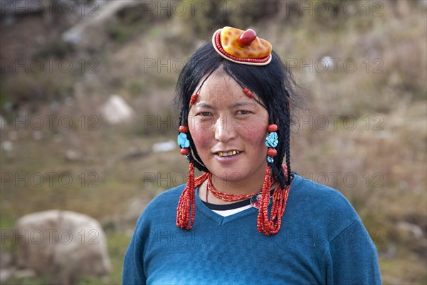 Portrait of Tibetan Khampa woman wearing traditional amber and red coral hair piece at Zhuqing