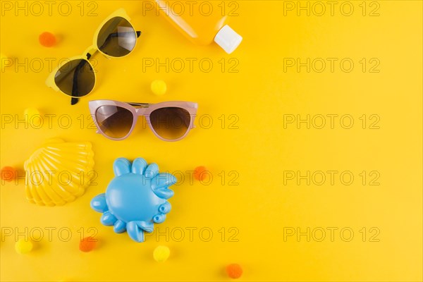 Overhead view sunglasses sunscreen lotion bottle scallop crab toy yellow backdrop