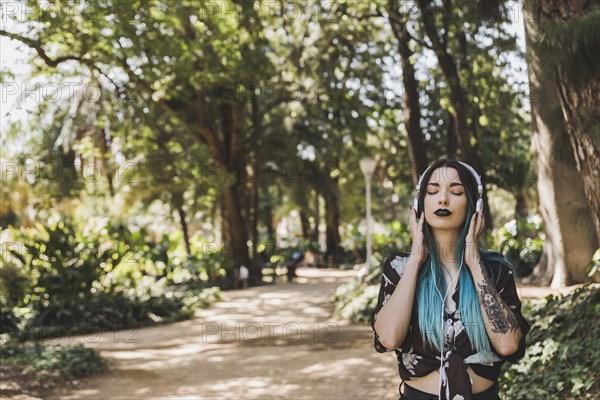 Woman with tattoo her hand enjoying music headphone standing park