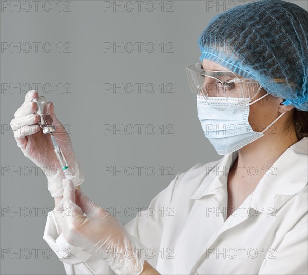 Side view female scientist with safety glasses hair net holding syringe