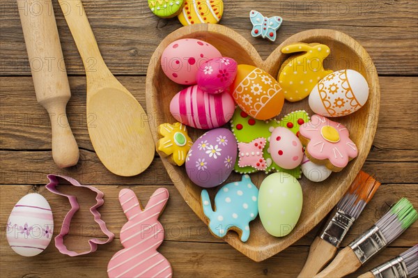 Top view colorful easter eggs heart shaped plate with kitchen utensils paint brushes
