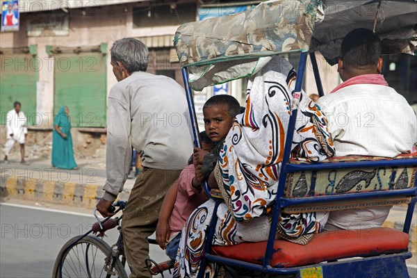 Cycle rickshaw with old driver transporting family as urban transport in Mathura