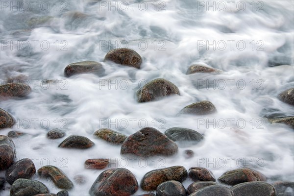 Close up of colourful cobbles covered by wave on shingle beach at rising tide