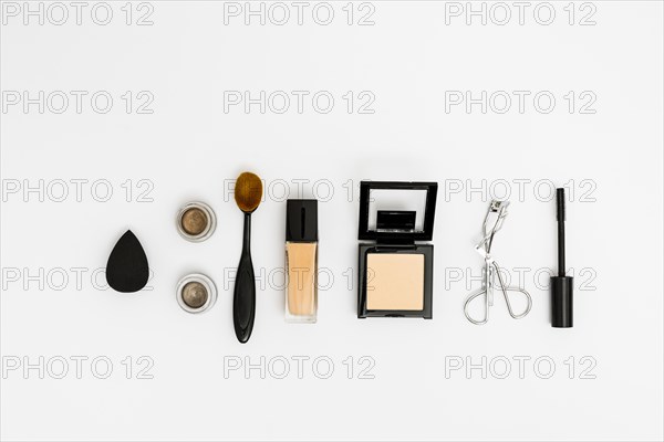 Overhead view blender eyeshadow oval brush compact powder eyelash curler mascara brush white backdrop