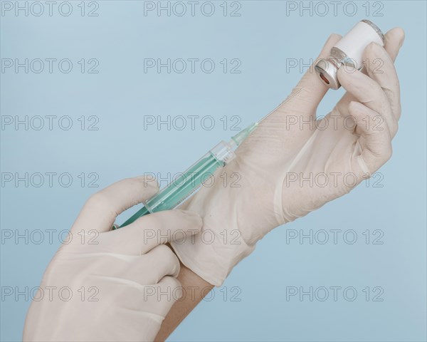 Hands with gloves holding syringe with vaccine bottle