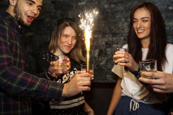 Young man holding lighted sparkle celebrating with friends