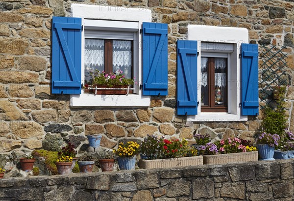 Windows with blue shutters and colourful flowers in front of a natural stone facade in Paimpol