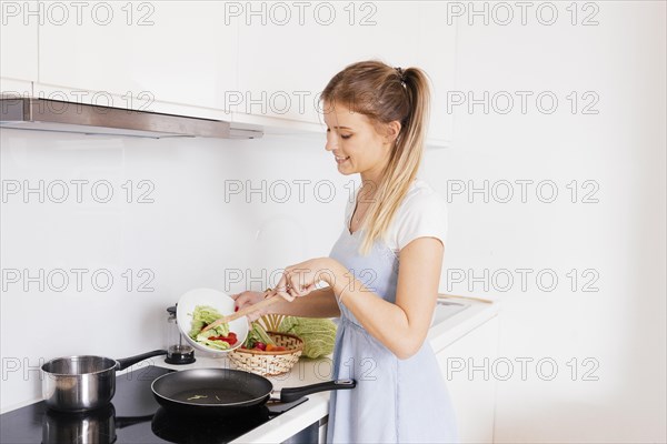 Smiling young woman cooking vegetables kitchen